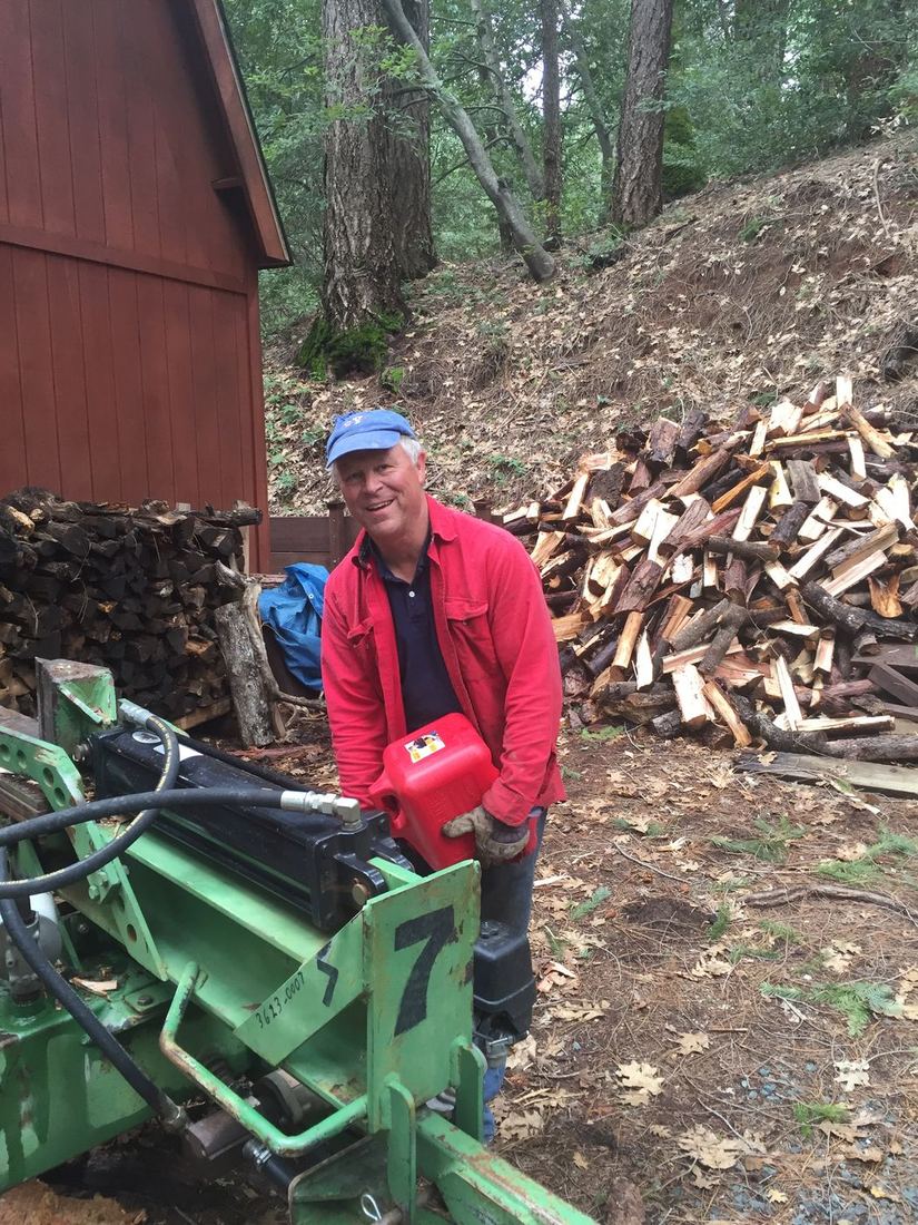 Terry splitting firewood in the woods beside a red cabin